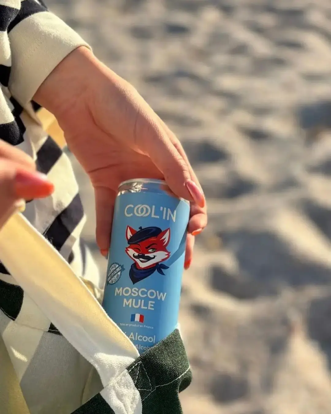 hugo spritz en canette, sur la plage tenue par la main d'une personne
